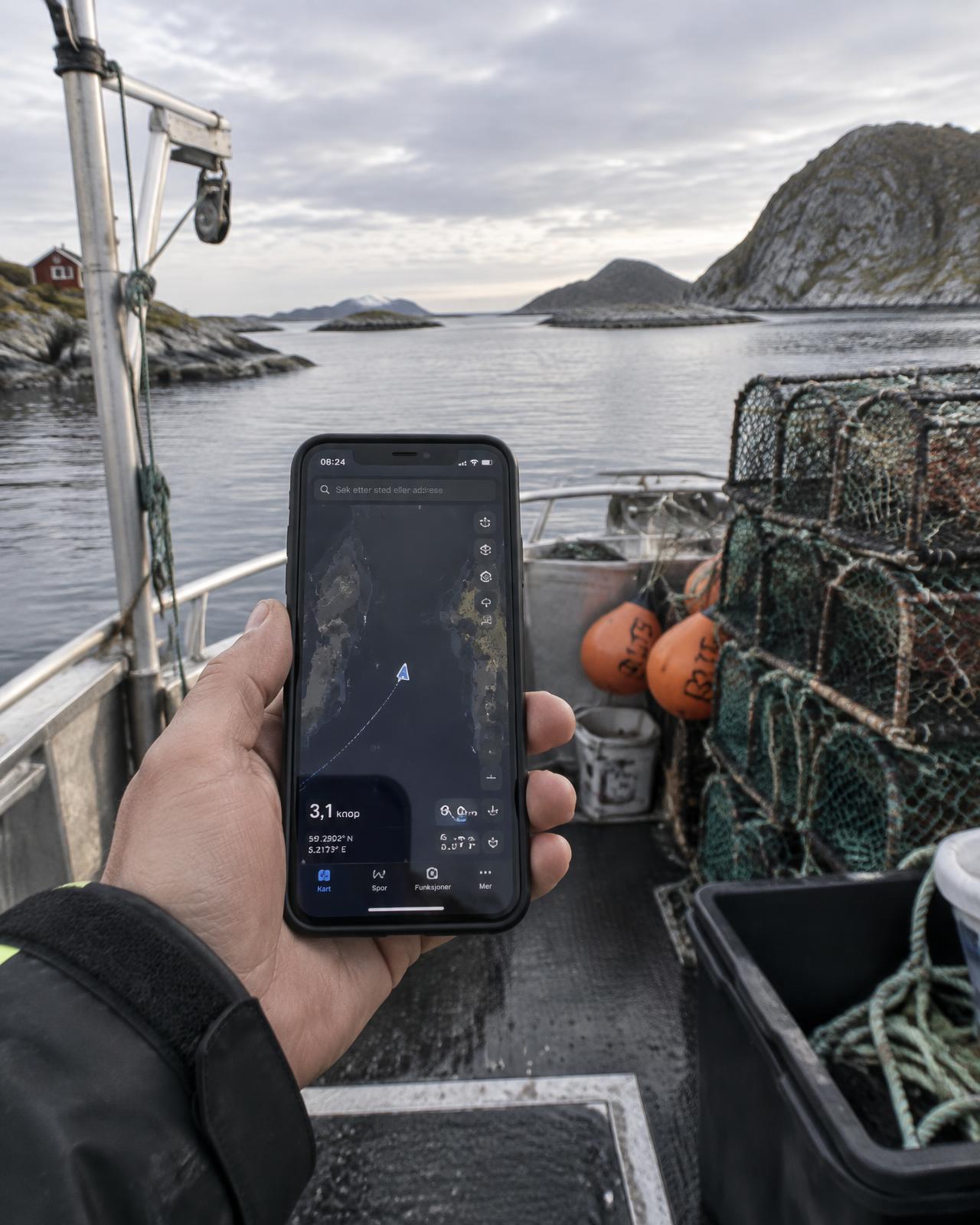 Fisker holder mobilen med SmartBouy-appen om bord i en båt med teiner på norskekysten